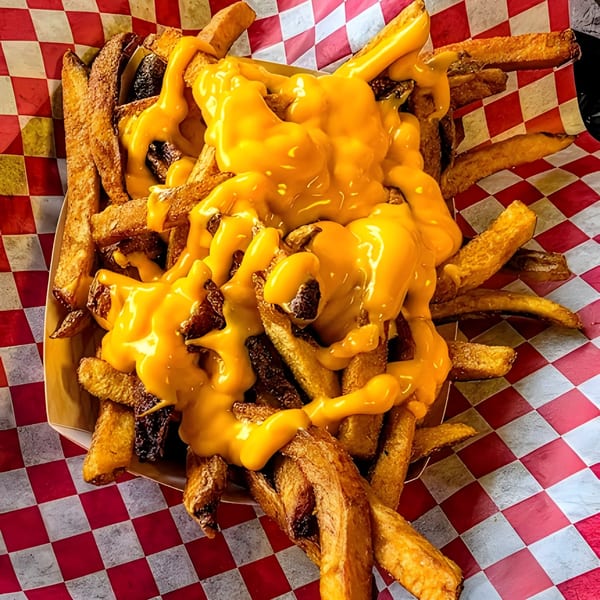 Golden-brown french fries generously topped with melted yellow cheese and bacon bits, served in a paper tray.