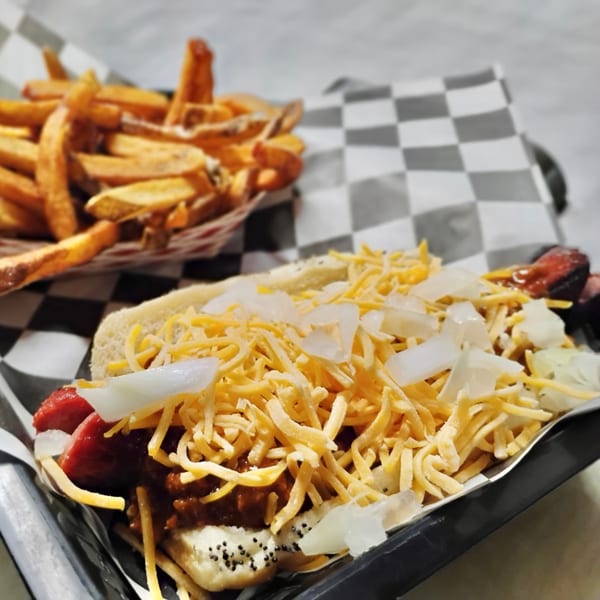 Chili cheese hot dog with onions and a side of french fries on a checkered paper.