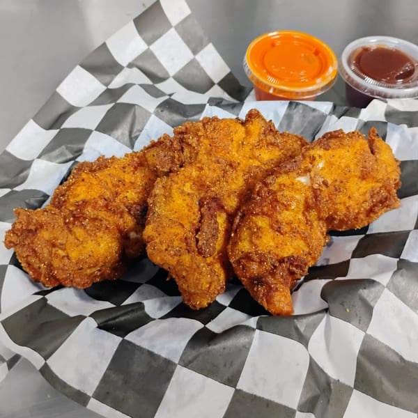 Crispy fried chicken tenders on checkered paper with two dipping sauces.