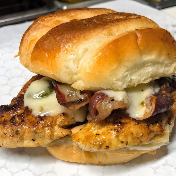 Grilled chicken sandwich with melted cheese, bacon, and caramelized onions on a toasted bun.